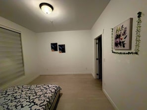 Ein Schlafzimmer mit einem Bett, einer Deckenleuchte, zwei Wandbildern und einer Tür zu einem anderen Raum.