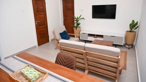 A modern living room with a sofa set, a TV mounted on the wall, and a wooden coffee table. - Lokko Serene One Bedroom (Accra)