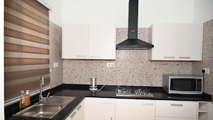 A kitchen with white cabinets, a stainless steel sink, a gas stove, a microwave, and a speckled backsplash. - Lokko Serene One Bedroom (Accra)