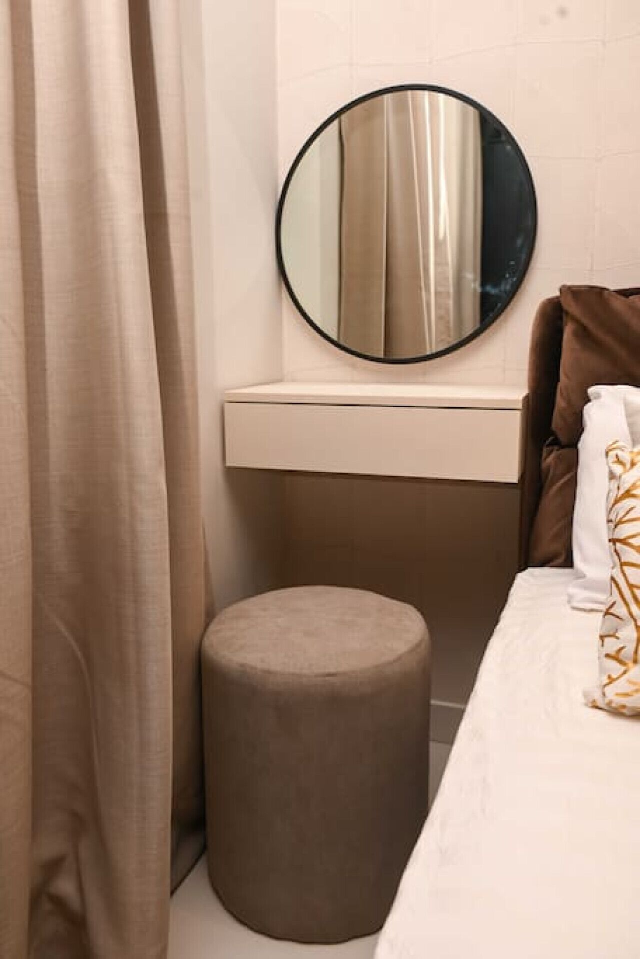 A bathroom with a round mirror, a small stool, and a bed with a brown headboard.