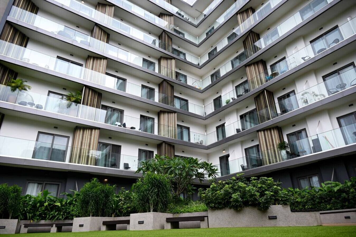 Un immeuble résidentiel à plusieurs étages, doté de balcons, de grandes fenêtres et d’un jardin bien entretenu.