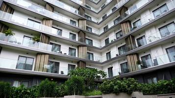 Un immeuble résidentiel à plusieurs étages, doté de balcons, de grandes fenêtres et d’un jardin bien entretenu.