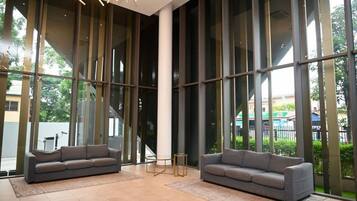 Un hall d’entrée spacieux, doté de grandes fenêtres, de deux canapés gris et d’un luminaire moderne.