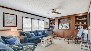 A living room with a blue sofa, a wooden coffee table, a TV, and a bookshelf. - ‘Beach Bay Pony Place’ w/ Ponies: 1 Mi to Water! (Chincoteague)