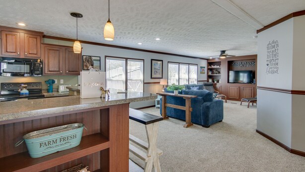 A kitchen with wooden cabinets, a microwave, and a farmhouse sink. There is a blue couch and a television in the living area. - ‘Beach Bay Pony Place’ w/ Ponies: 1 Mi to Water! (Chincoteague)