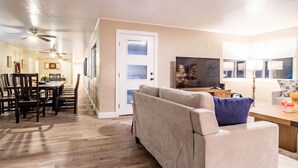 A living room with a beige sofa, wooden dining table, and chairs. There is a TV on the wall and a ceiling fan. - Ultimate Relaxation Retreat w/ Game Room & Hot Tub (Ahwahnee)