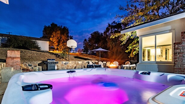 A hot tub with a stone wall backdrop, a basketball hoop, and outdoor seating. - Ultimate Relaxation Retreat w/ Game Room & Hot Tub (Ahwahnee)