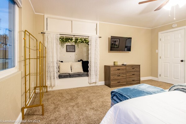 A bedroom with a window seat, a bed, a dresser, and a ceiling fan.