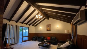 Un vaste salon doté d’un haut plafond, de poutres apparentes, d’un lustre et d’une grande porte-fenêtre coulissante donnant sur un espace extérieur.