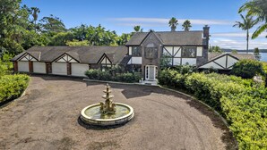 Une grande maison avec une allée, une fontaine et une vue sur l’eau.