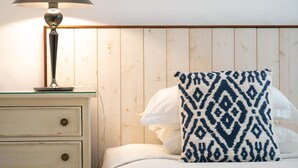 Un lit avec un oreiller blanc et un autre à motifs, une table de chevet avec une lampe et un mur en bois.