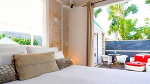 Een slaapkamer met een groot bed, een balkon met wit rieten meubilair en uitzicht op groen.