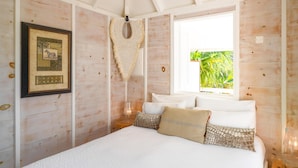 Een slaapkamer met een groot bed, een macramewerk aan de muur, een ingelijste foto en een raam met uitzicht op groen.