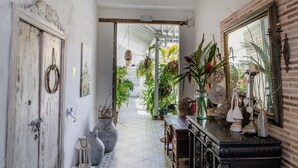 Un couloir avec des carreaux de sol à motifs, un lustre, un miroir et divers objets décoratifs.