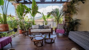 Une terrasse couverte avec un canapé, des tables rondes et des plantes en pot.