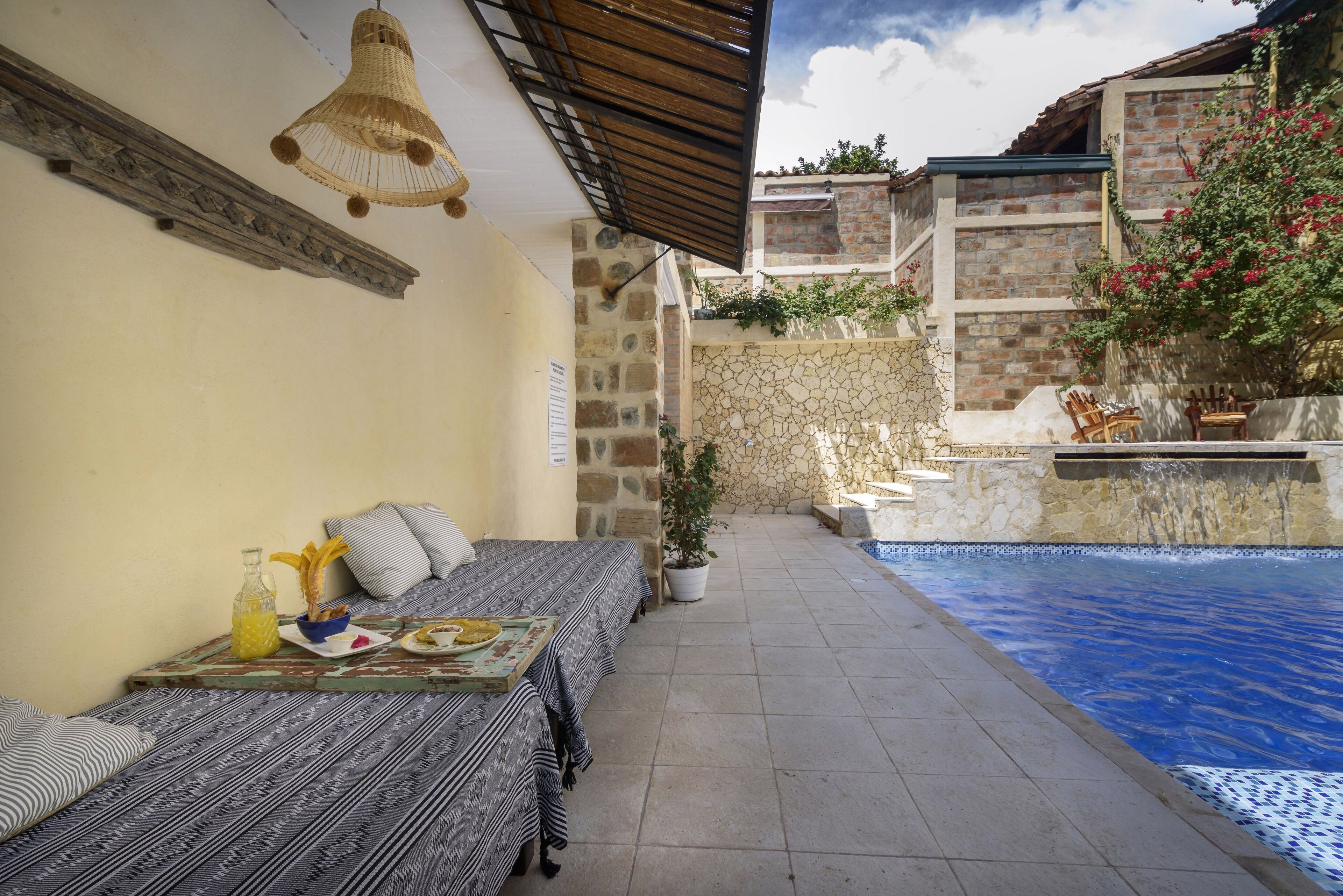 A patio with a pool, a table with a bottle and a bowl, and a sofa with patterned cushions.