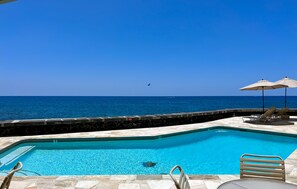 A swimming pool with a view of the ocean, lounge chairs, and umbrellas.