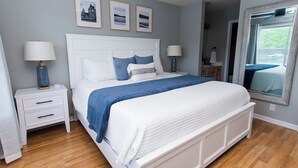 A bedroom with a bed, nightstands, a ceiling fan, framed pictures on the wall, and a window with blinds.