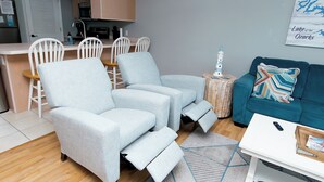 A modern living room with a sofa, a coffee table, and a dining area with chairs and a kitchen in the background.