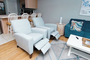 Un salon moderne avec un canapé, une table basse et un coin repas comprenant des chaises, et une cuisine en arrière-plan.