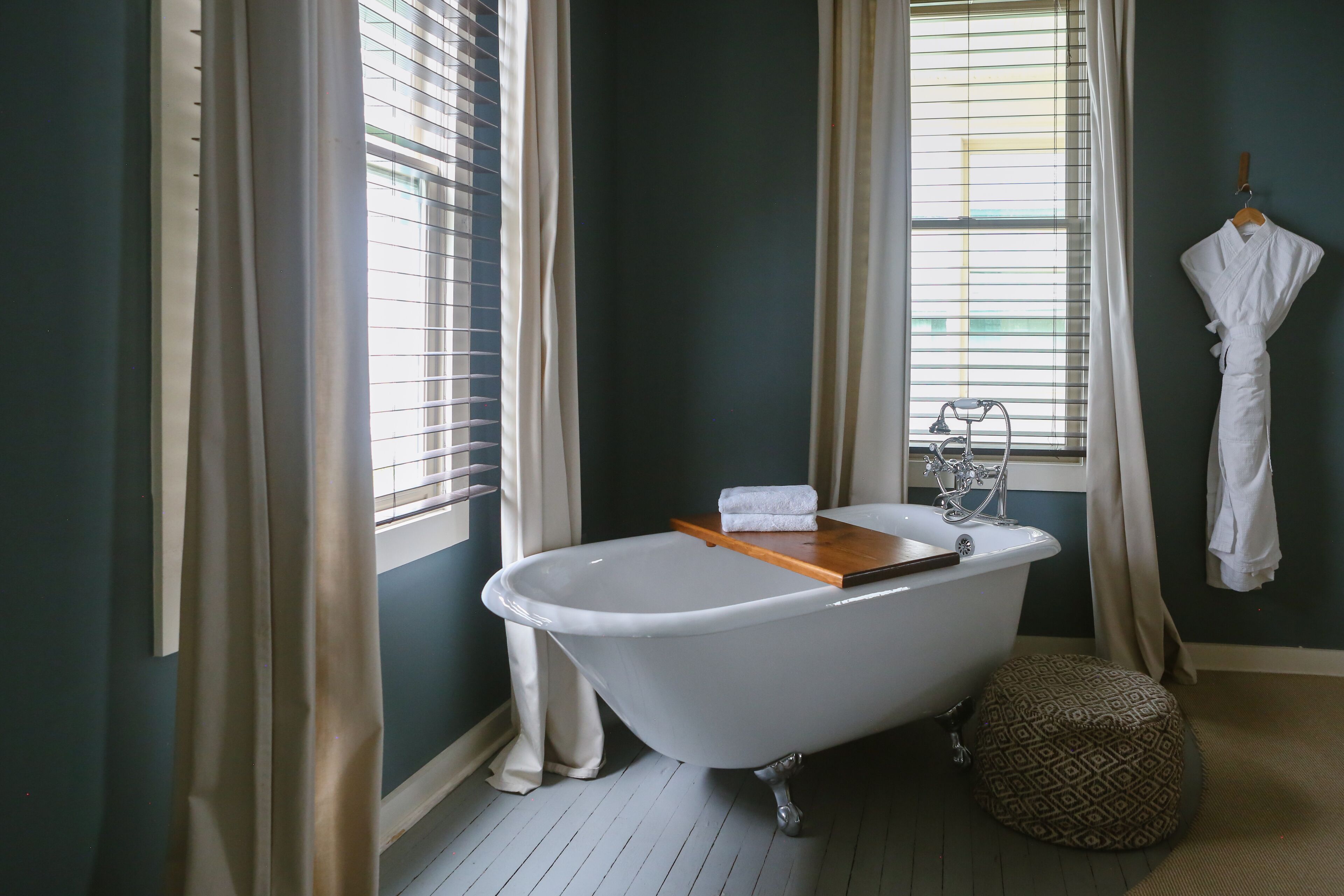A bathroom with a freestanding bathtub, a wooden tray, a towel, and a patterned ottoman.