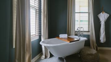 A bathroom with a freestanding bathtub, a wooden tray, a towel, and a patterned ottoman.