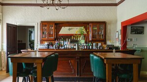 A bar area with wooden cabinets, a counter with various bottles, and green chairs. - The North Branch Inn (North Branch)