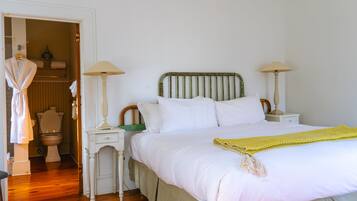 Ein Schlafzimmer mit einem Bett, zwei Nachttischen, einer Stehlampe, einem Kleiderhaken und einer Toilette, die durch eine offene Tür zu sehen ist.