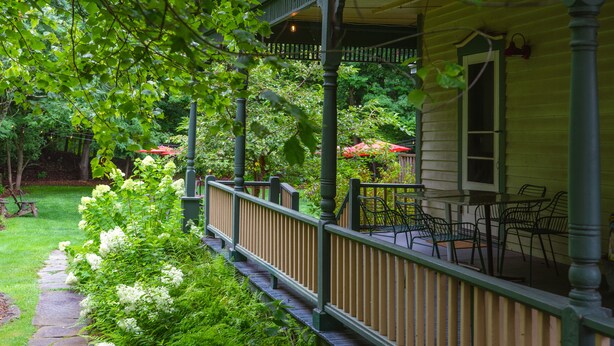 A covered porch with outdoor seating, surrounded by lush greenery and a stone pathway. - The North Branch Inn (North Branch)