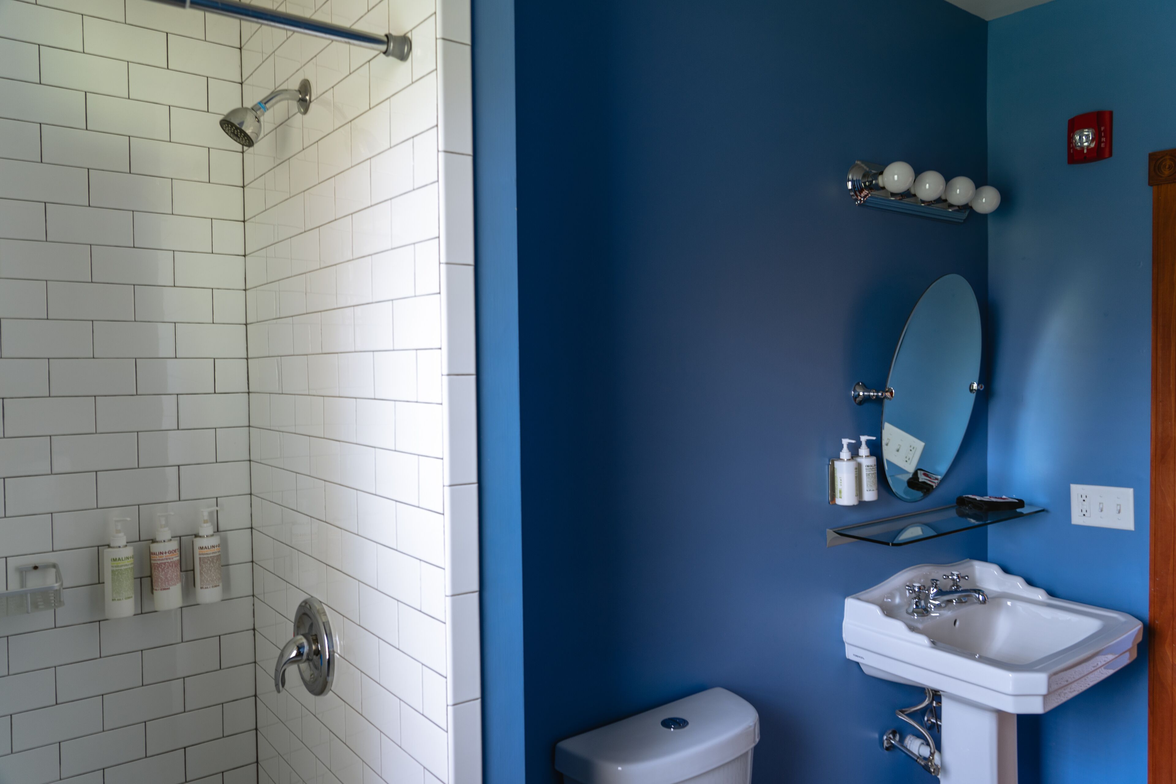 A bathroom with white tiled walls, a blue accent wall, a white sink, a mirror, and toiletries on the wall.
