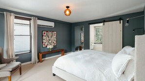 A bedroom with a large bed, a chair, a bedside table, and a wall-mounted lamp. - The North Branch Inn (North Branch)