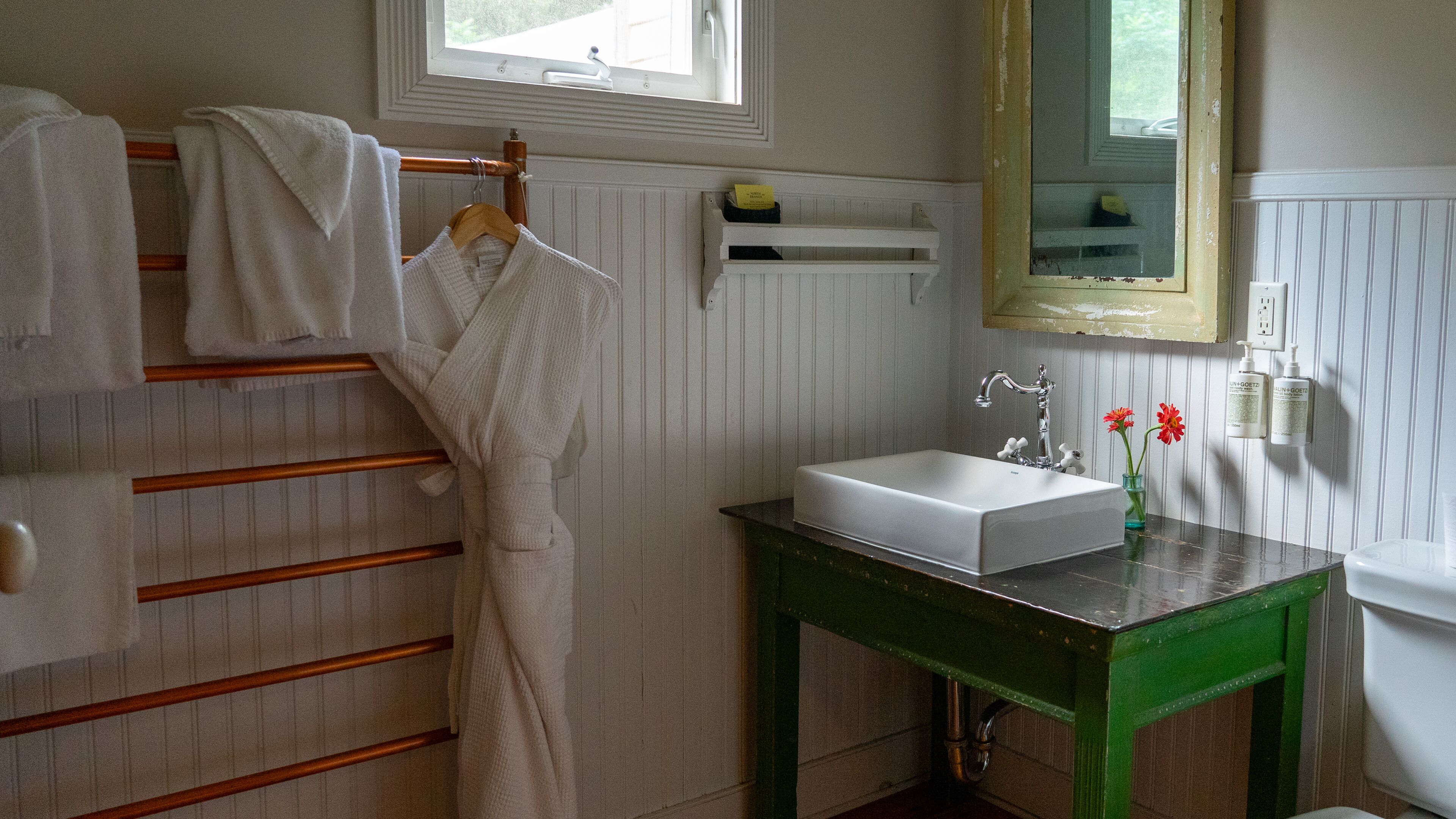 A bathroom with a white bathtub, a green vanity with a sink, and a towel rack with white towels.