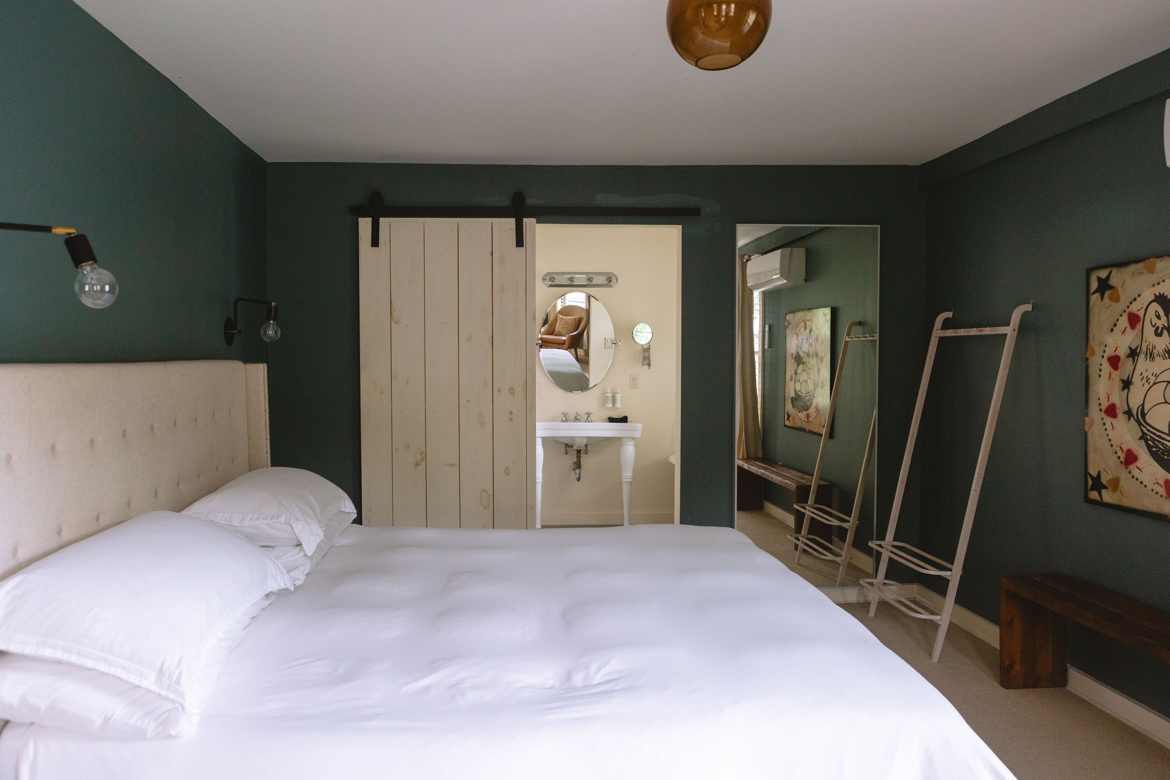 A bedroom with a bed, a white dresser, a mirror, a white sink, and a ladder.