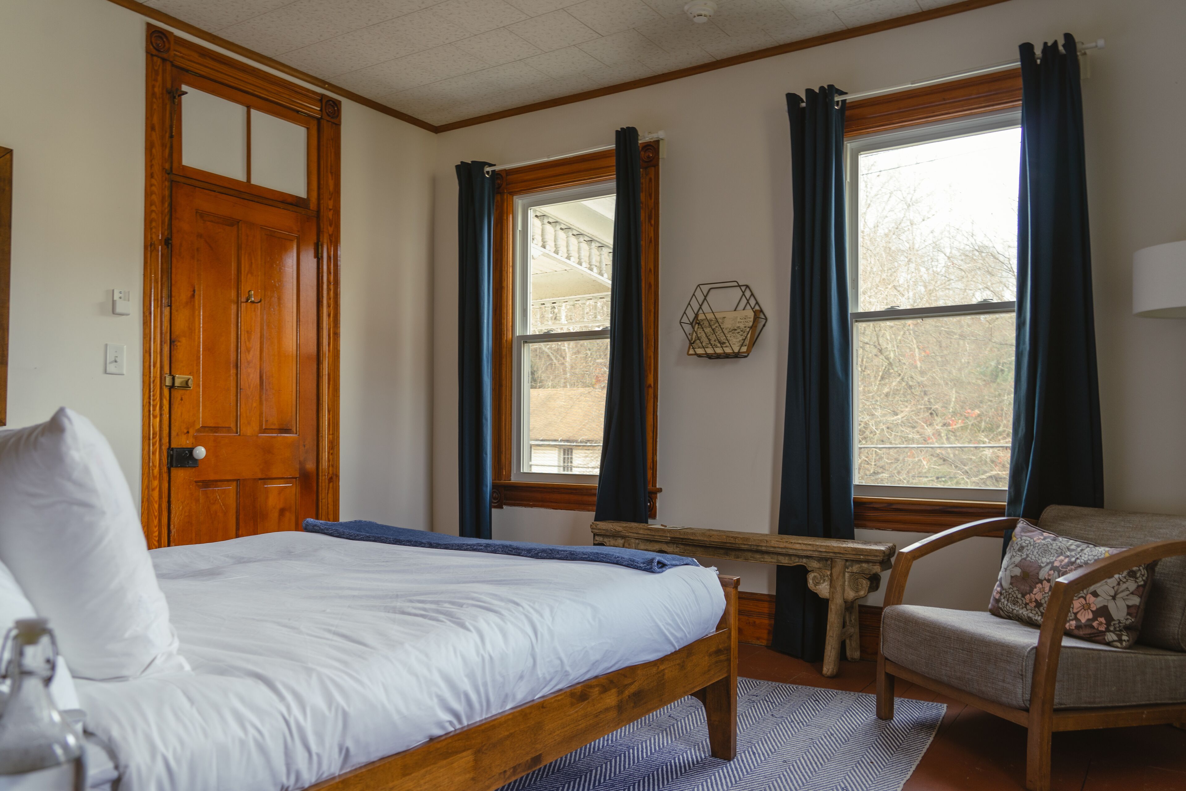 A bedroom with a wooden bed, a chair, a small table, and a window with curtains.