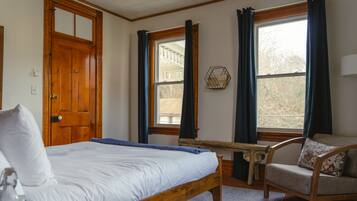 A bedroom with a wooden bed, a chair, a small table, and a window with curtains.