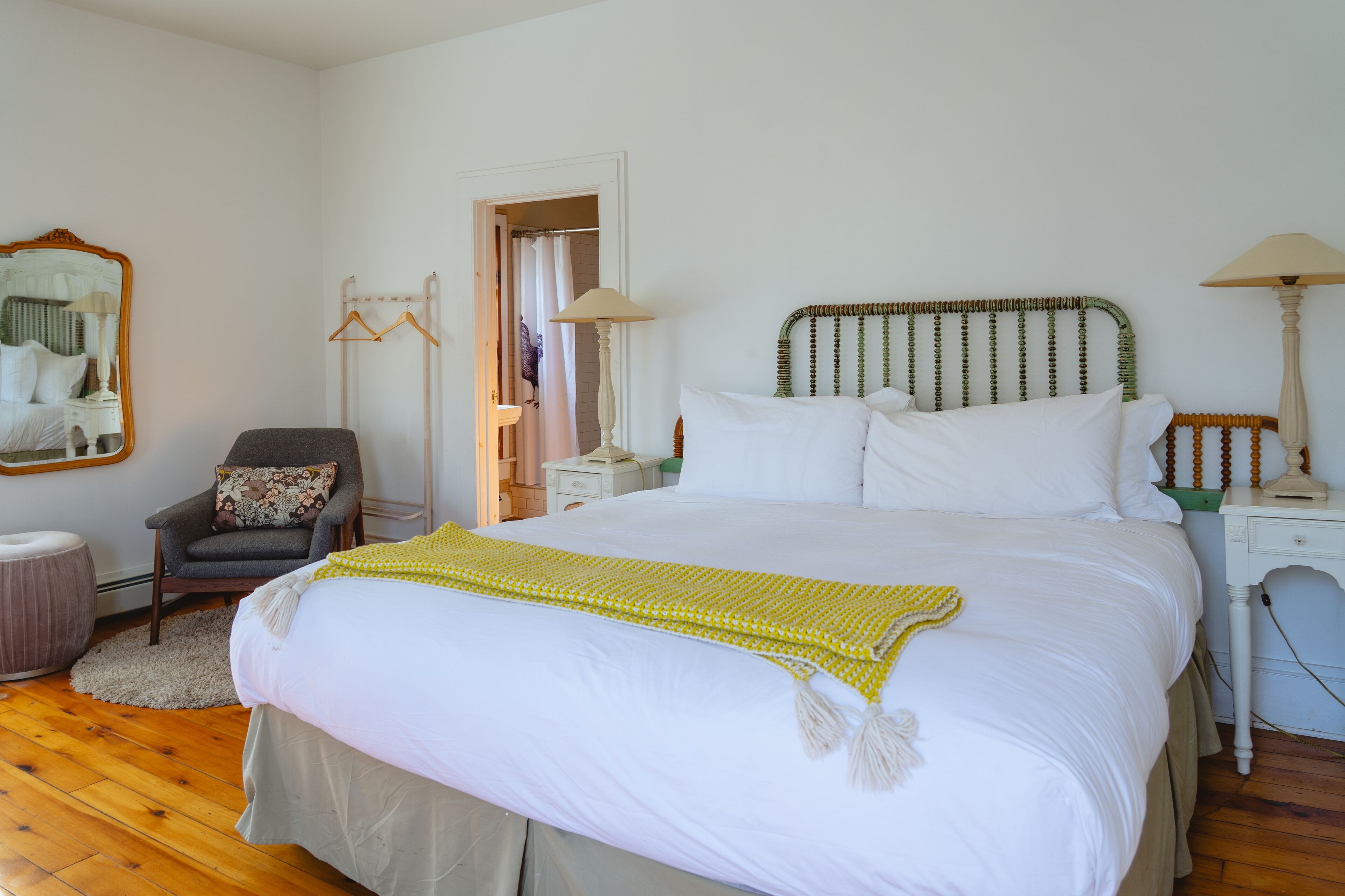 A bedroom with a large bed, a chair, a nightstand, a lamp, and a mirror.