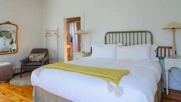 A bedroom with a large bed, a chair, a nightstand, a lamp, and a mirror.