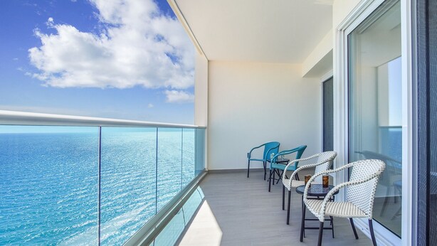 A balcony with a view of the ocean, featuring two wicker chairs and a small table.
