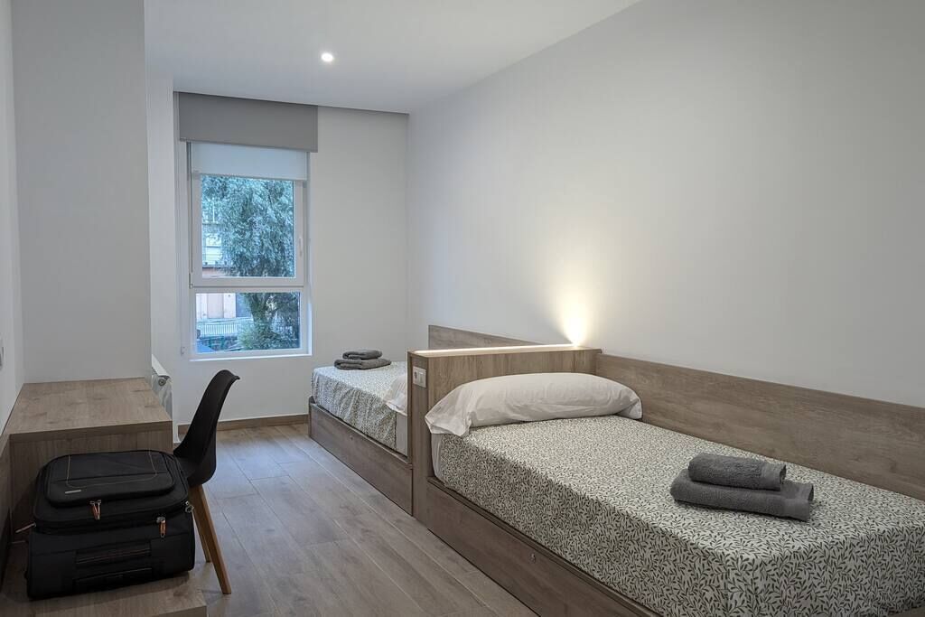 A small, modern bedroom with a single bed, a desk, and a chair.