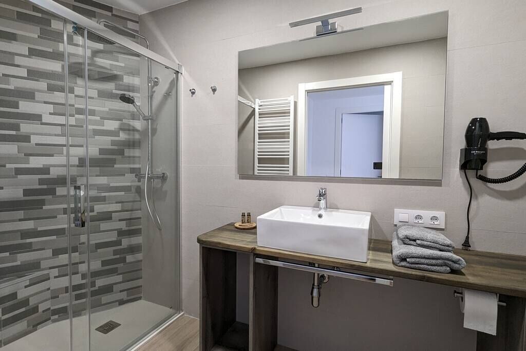 A modern bathroom with a glass shower enclosure, a white sink, and a towel rack.
