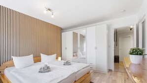 A modern bedroom with a wooden headboard, a double bed, a wardrobe, a mirror, and a small plant. - Bahnhofstraße 10 - Wohnung 4 - Moderne und Familienfreundliche Ferienwohnung in Zentrumsnähe (Zingst)