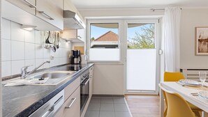 A modern kitchen with a built-in oven, a coffee maker, and a window overlooking a house. - Bahnhofstraße 10 - Wohnung 4 - Moderne und Familienfreundliche Ferienwohnung in Zentrumsnähe (Zingst)