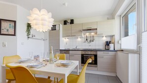 A modern kitchen with a dining area, featuring a white table, yellow chairs, and a pendant light. - Bahnhofstraße 10 - Wohnung 4 - Moderne und Familienfreundliche Ferienwohnung in Zentrumsnähe (Zingst)