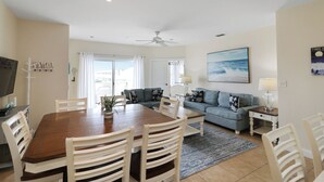 A modern living room with a dining area, a sofa set, a ceiling fan, and a TV. - Oceanfront Condo with Pool & Stunning Beach Views (Tybee Island)