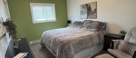 A bedroom with a bed, a desk, a chair, a rug, a ceiling fan, and a window with blinds.