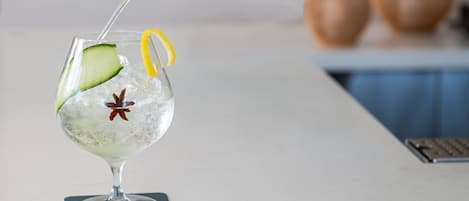 A hand pouring a clear liquid into a glass with a cucumber slice and star anise.