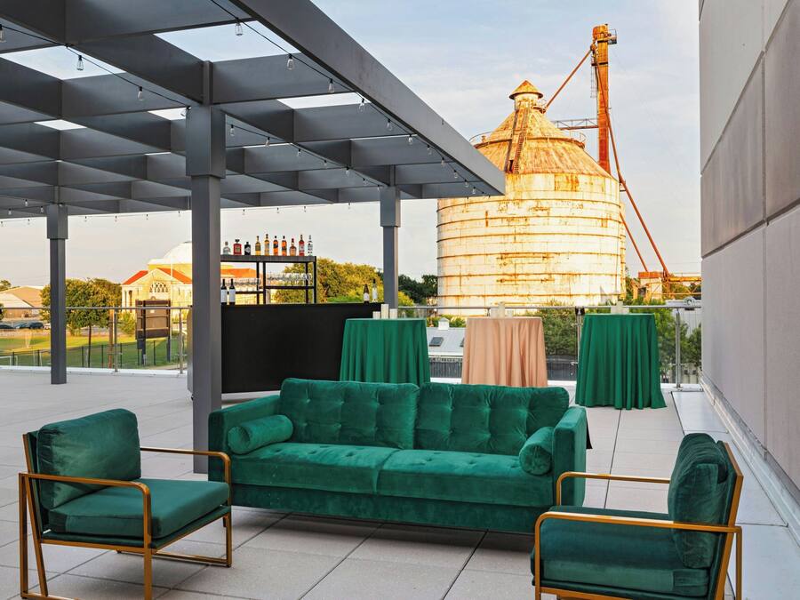Un área de estar al aire libre con un sofá y sillas verdes, una pérgola y vistas de un edificio industrial grande.
