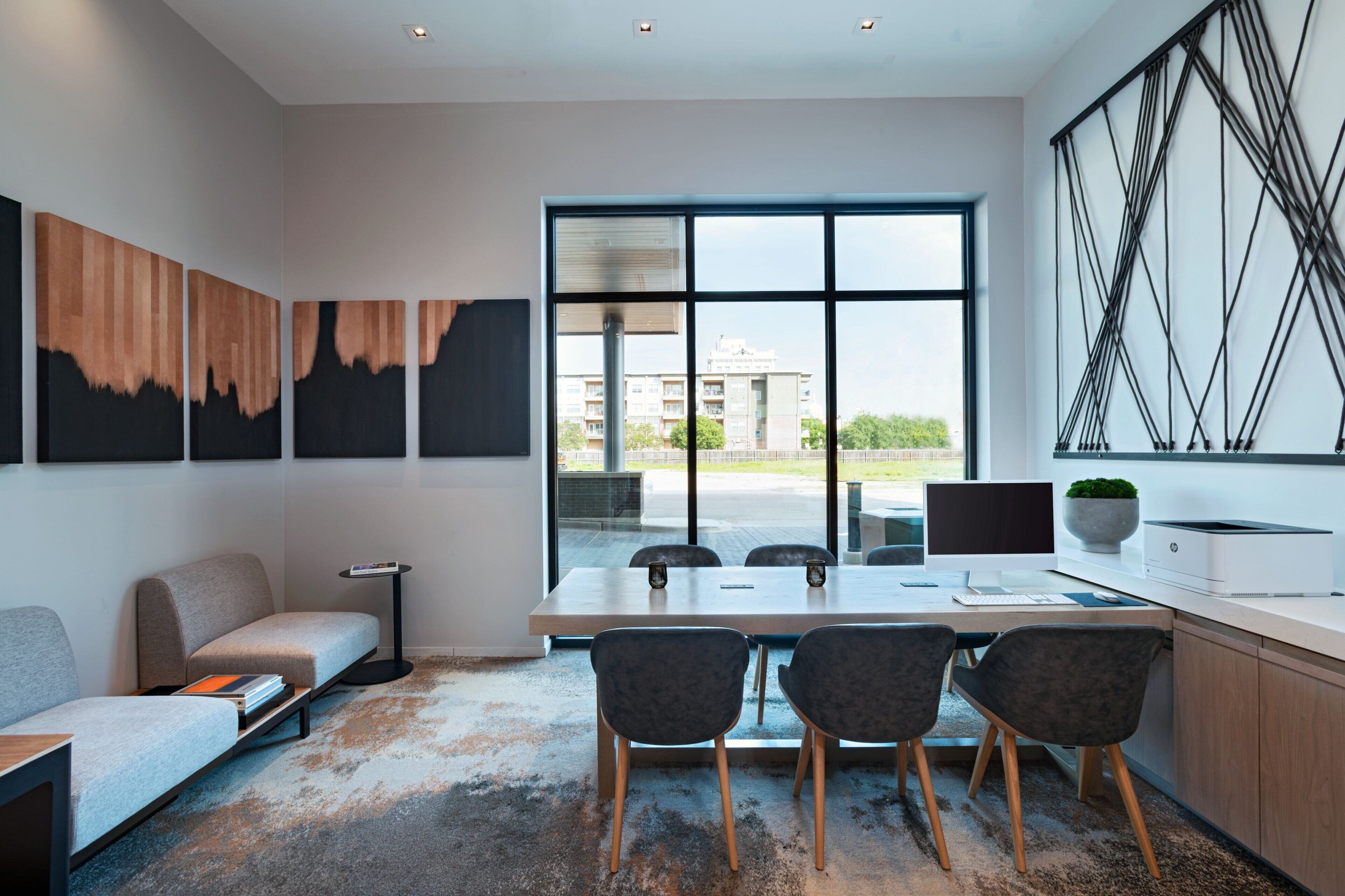 A modern office space with a large table, four chairs, a sofa, and artwork on the walls.