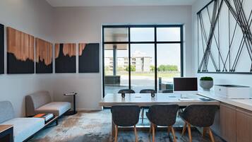 A modern office space with a large table, four chairs, a sofa, and artwork on the walls.