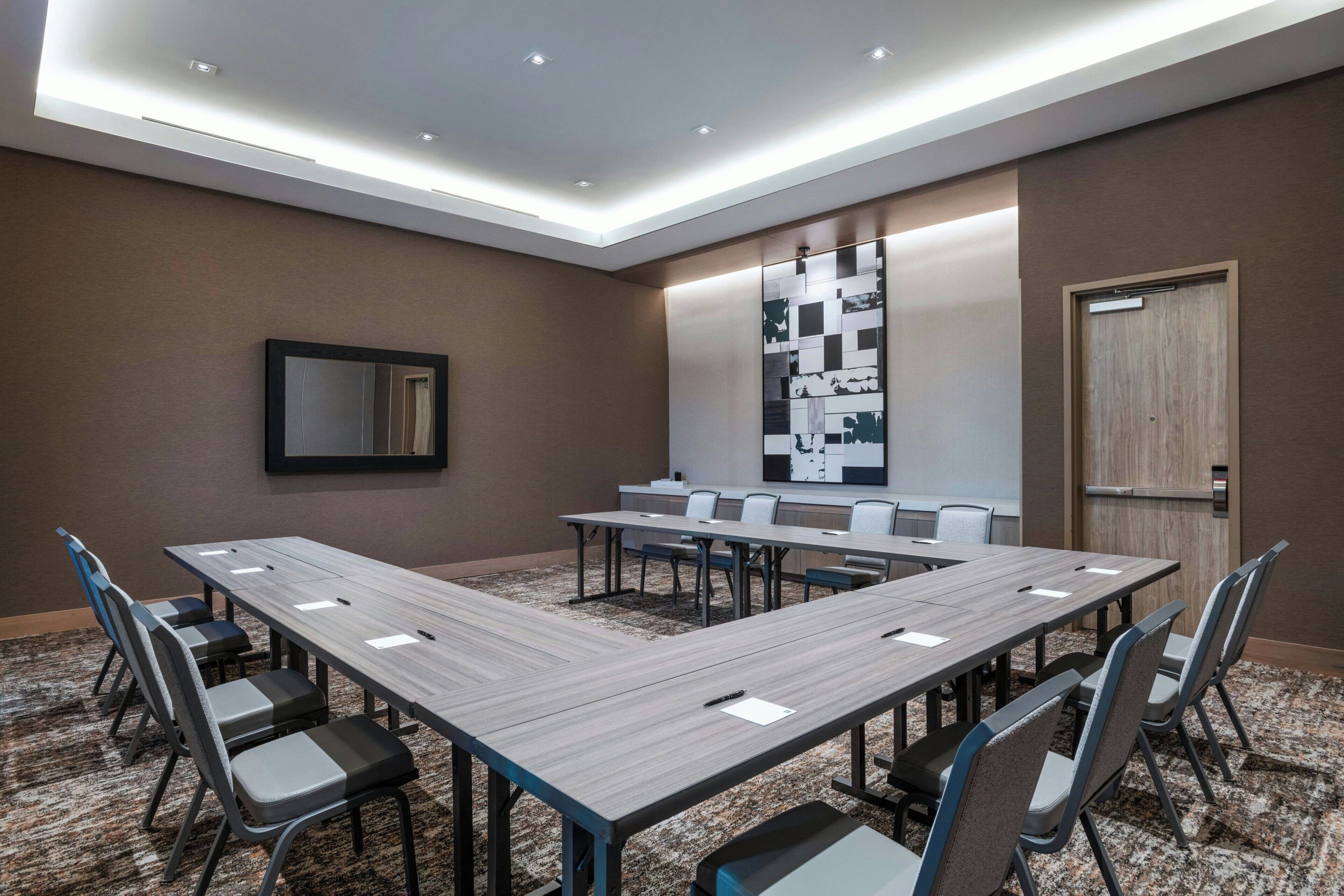 A conference room with a long table, chairs, a large mirror, and a wall with a geometric pattern.